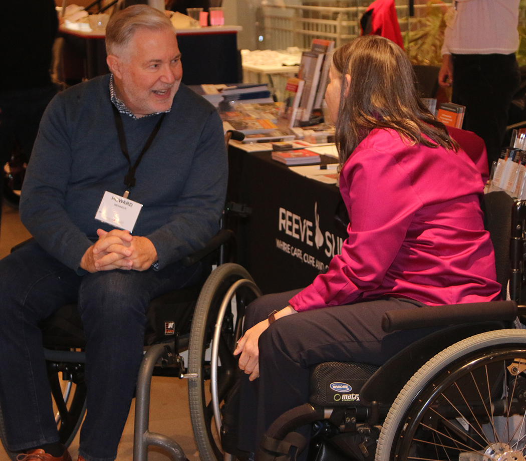 Two wheelchair users at a Reeve Foundation information table