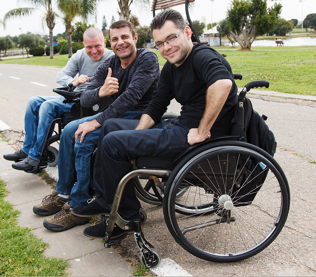Three men in wheelchairs smiling and one giving thumbs up.