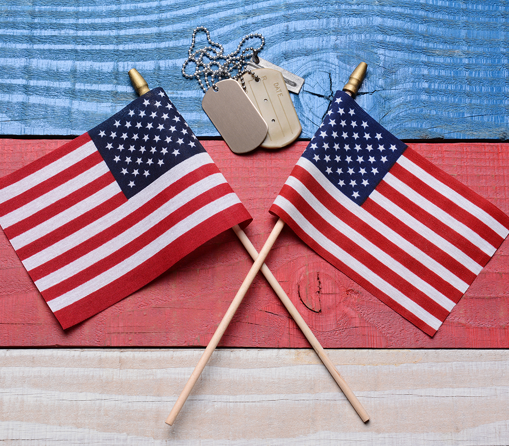Two crossed American flags on a red, white and blue wood table with military dog tags. Great concept image for the 4th of July, Memorial Day, Veterans Day or military projects.