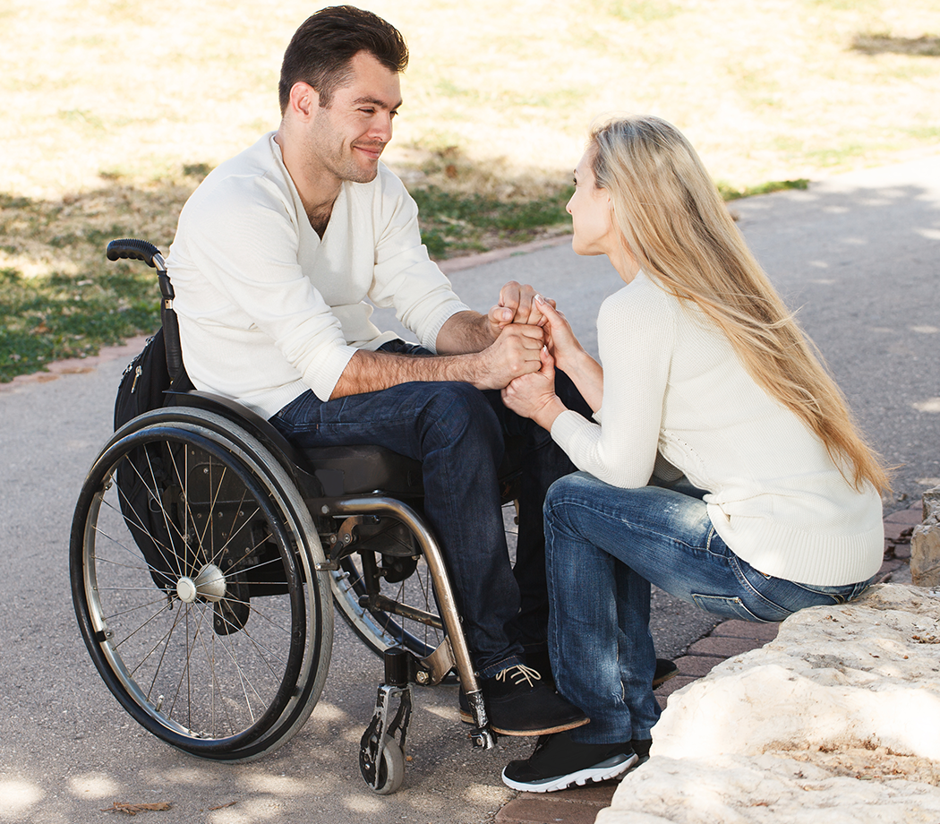 Young disabled man on a wheelchair talking with his girlfriend in the park
