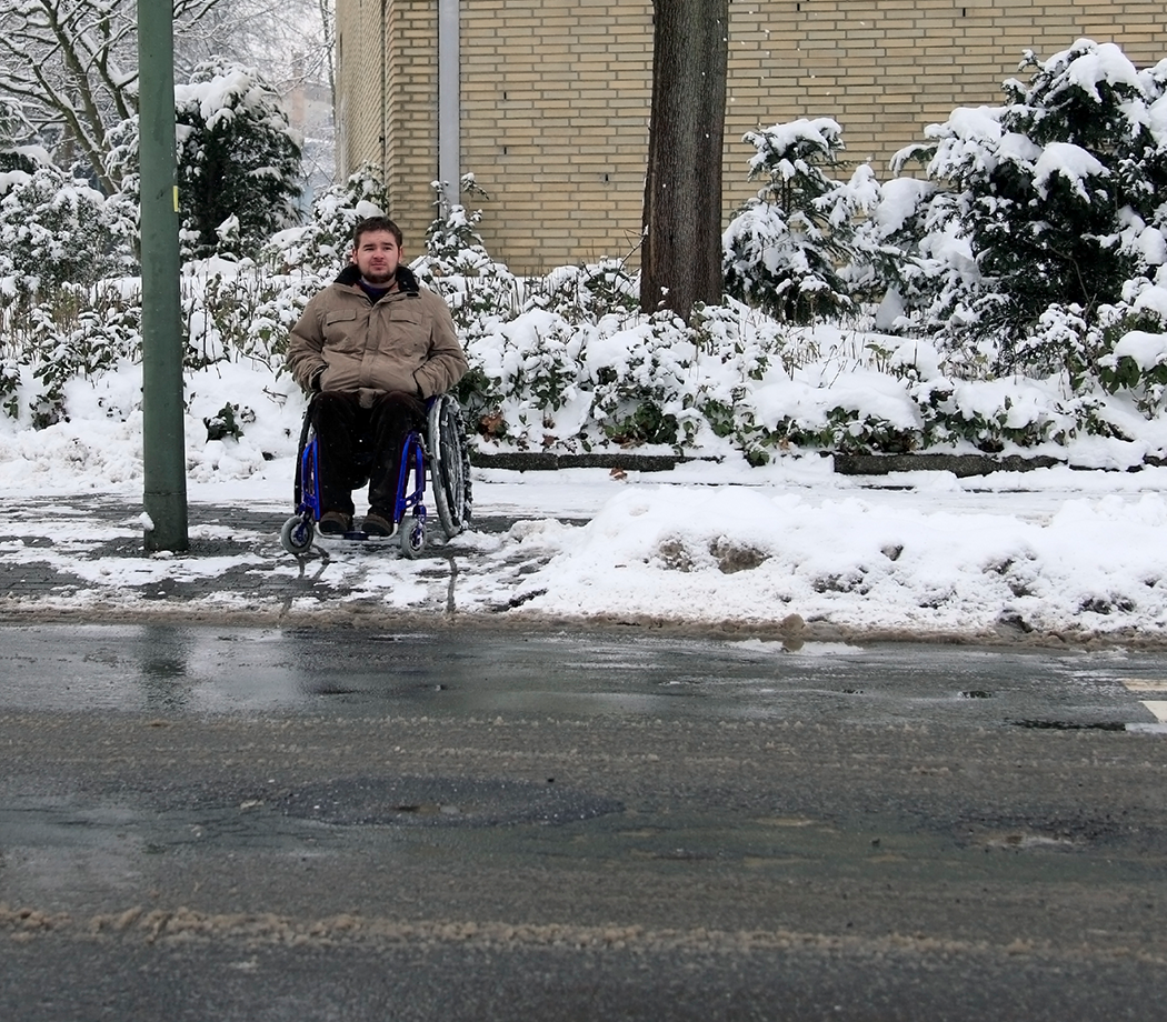 young man in wheelchair at a traffic light waiting for help to cross the street