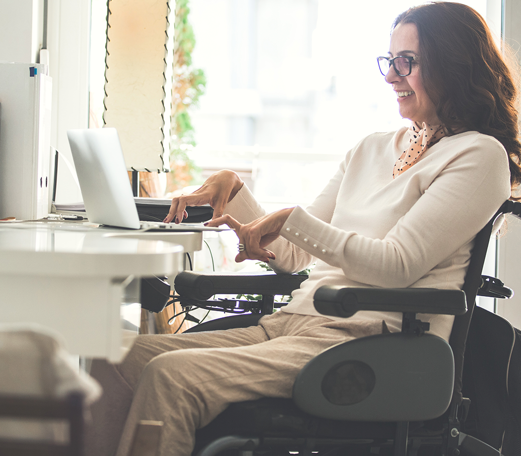 Side view of a happy woman with physical disability working on a laptop in the office.