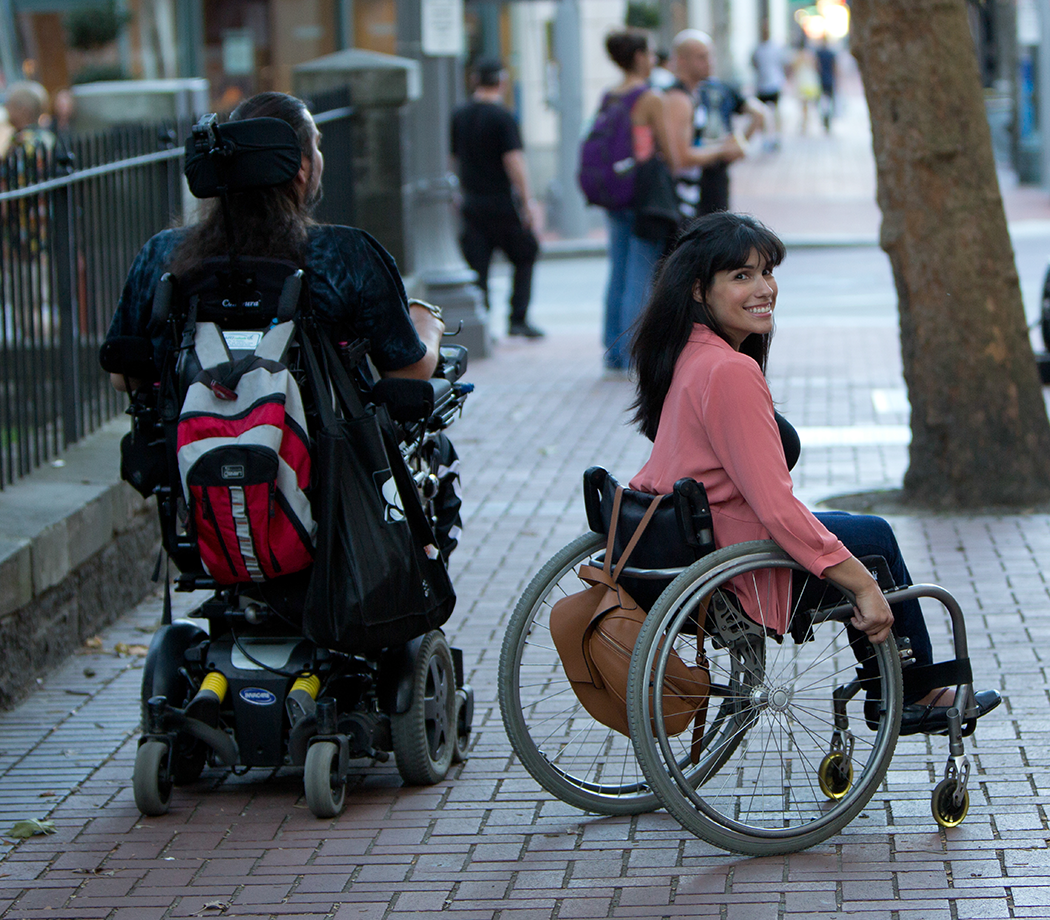 Person in a power wheelchair and a woman in a manual wheelchair on a sidewalk