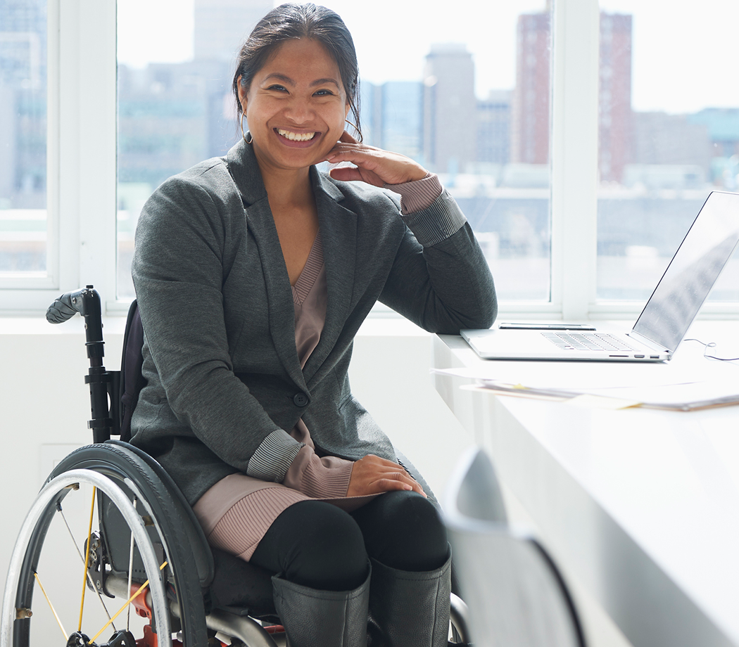 Woman in wheelchair smiling at desk with laptop
