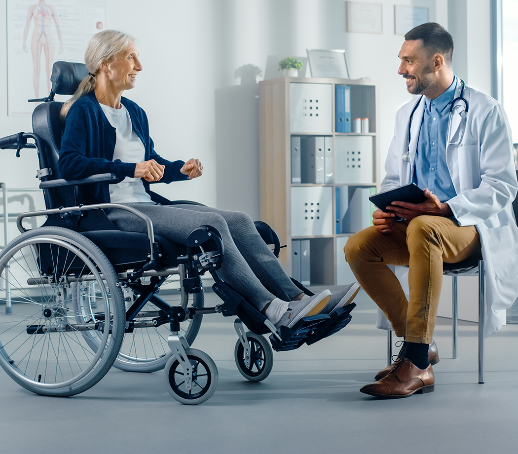 Hospital Physical Therapy: Strong Senior Female in Wheelchair, Talks to a Friendly Rehabilitation Physiotherapist Doctors Gives Advice, Plans Rehabilitation Treatment for Determined Disabled Patient