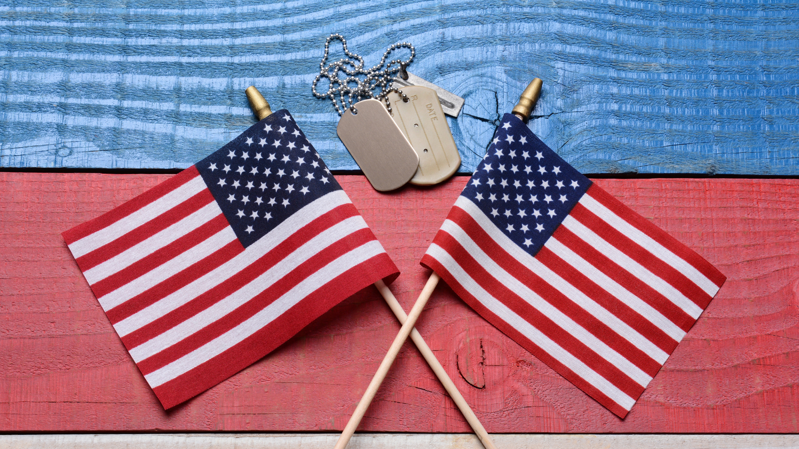 Two crossed American flags on a red, white and blue wood table with military dog tags.